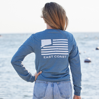 Person wearing a Connecticut blue '203' long-sleeve shirt with 'East Coast' design by the water