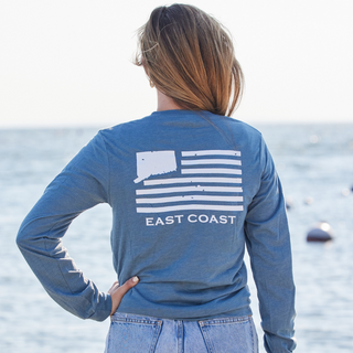 Person wearing a Connecticut blue '203' long-sleeve shirt with 'East Coast' design by the water